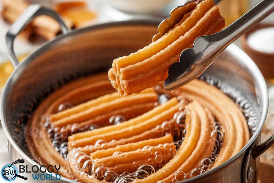 Perfectly fried churros frying in a saucepan with bubbling oil.