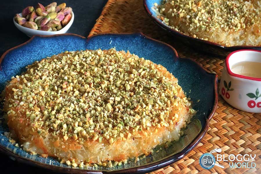 delicious Turkish dessert kunafah served in a dish topped with crushed pistachios sugar syrup and pistachio also served seperately for additional sweetness