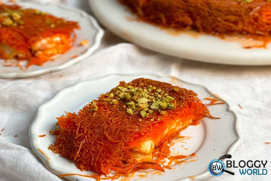 a slice of palestinian dessert kunafah is served in a plate dusted with crushed pistachios image presented by blloggy world